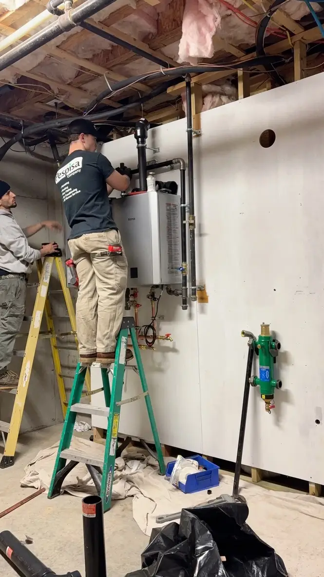 Technicians on ladders installing wall-mounted heating equipment and copper piping