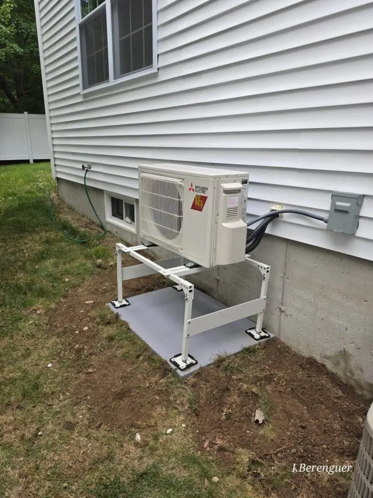 Mitsubishi outdoor heat pump on a raised stand beside a Littleton, MA home