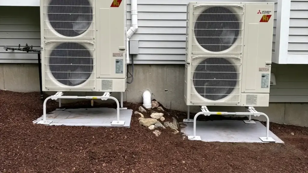 Two Mitsubishi Hyper-Heat outdoor units installed side by side on raised stands at a Massachusetts home