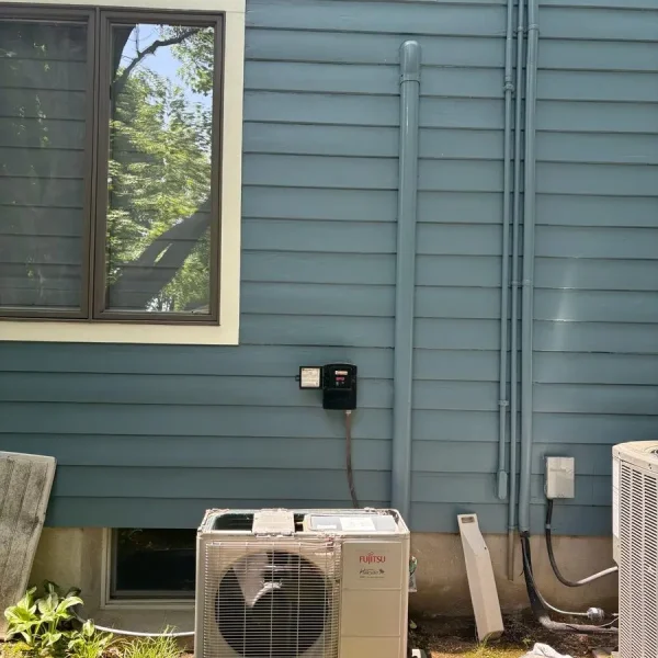 Fujitsu outdoor mini-split condenser during HVAC service beside a residential property
