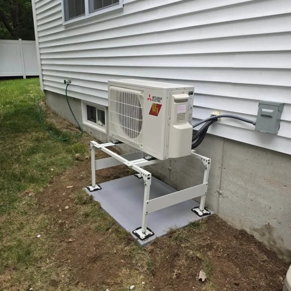 Mitsubishi outdoor heat pump on a raised stand beside a Littleton, MA home
